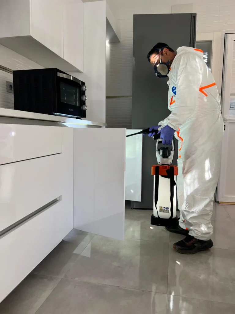 Aplicación del tratamiento contra cucarachas debajo de un armario de la cocina